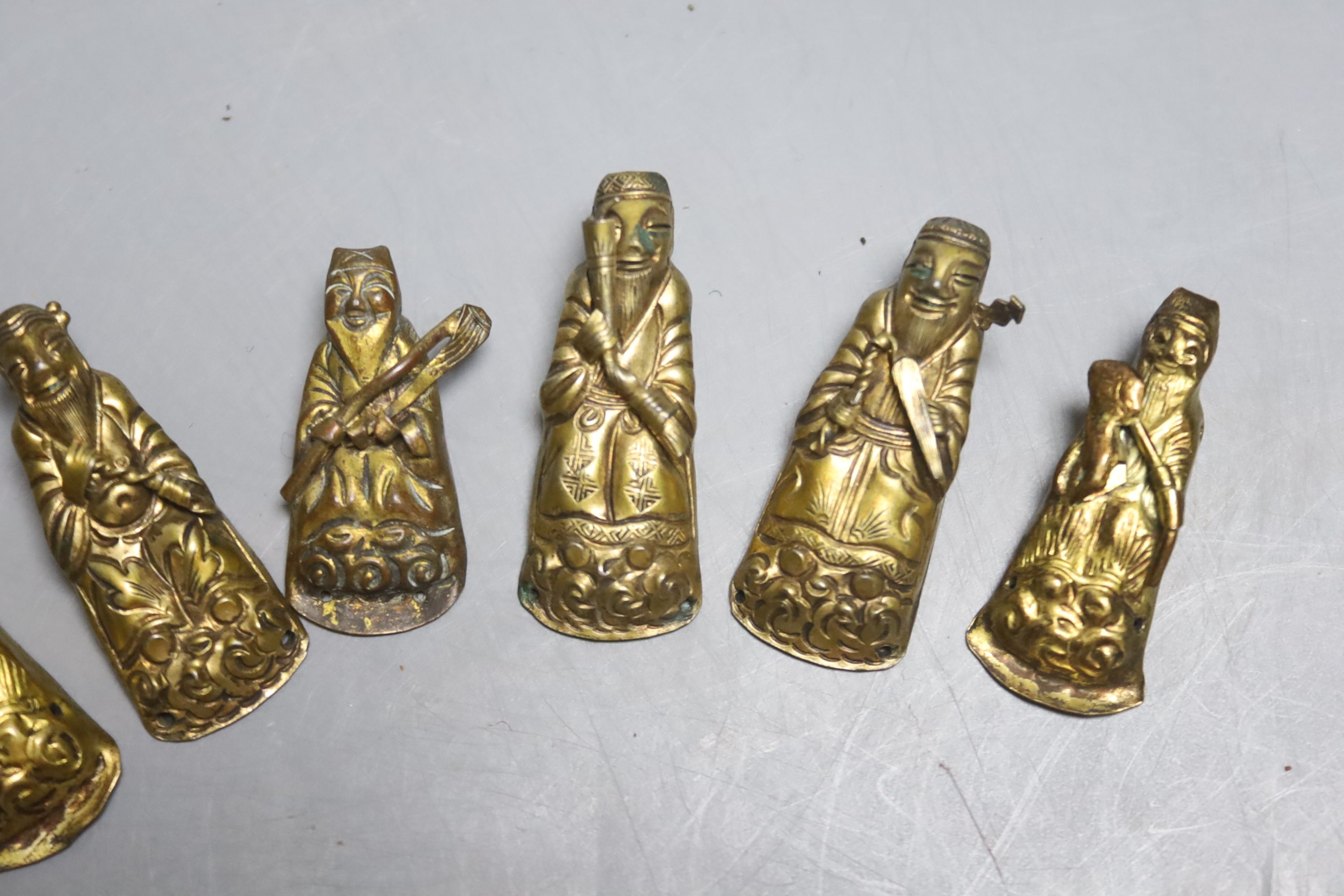 A group of eight Chinese figural pressed metal figural mounts in the form of sages, each 3.5cm. long.